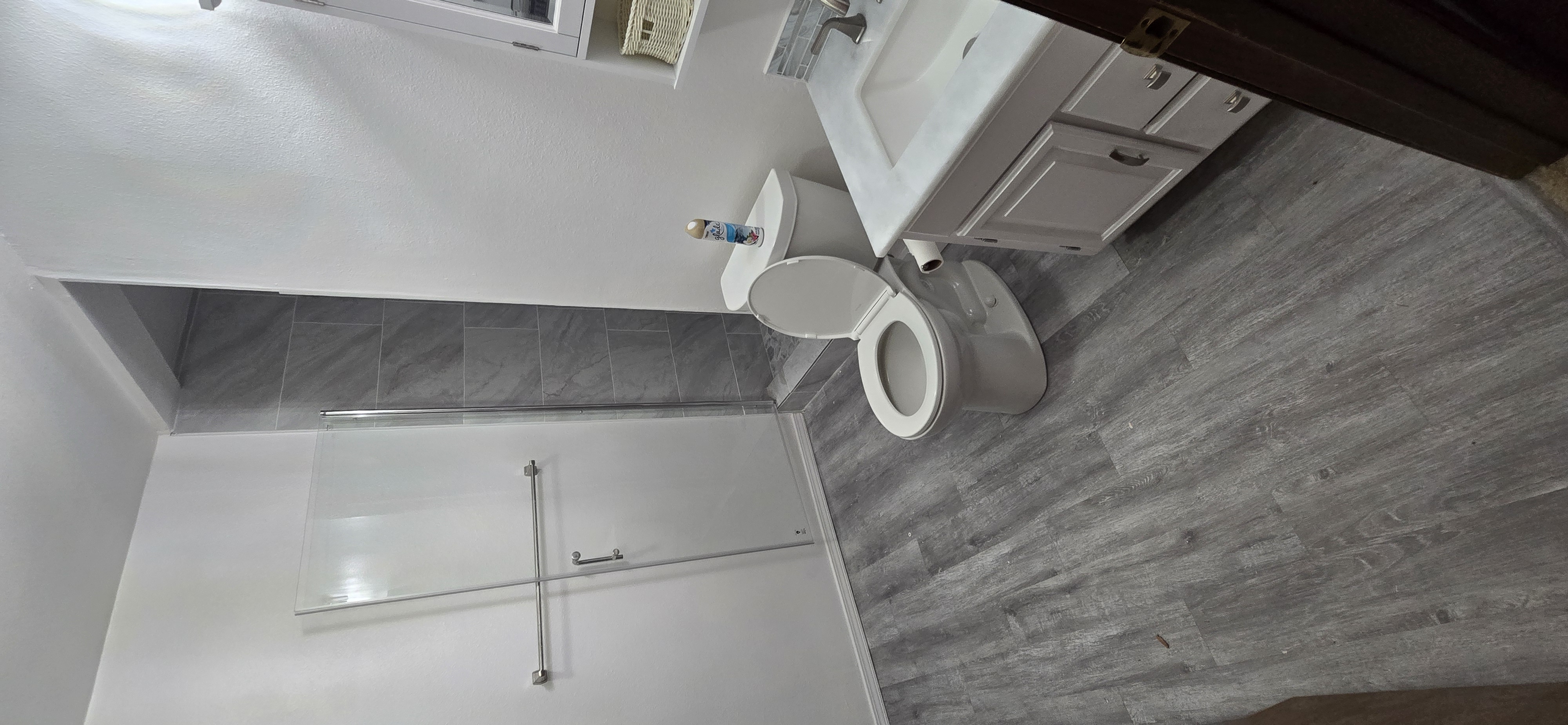 Finished bathroom after remodel — white vanity, glass shower door, gray tile